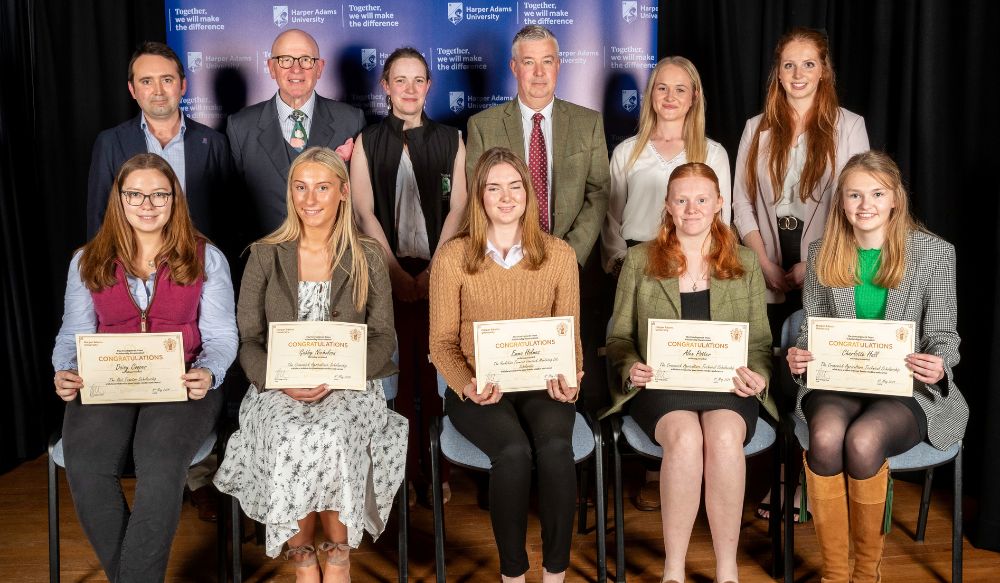 Eleven people split between two rows posing for photo holding certificates